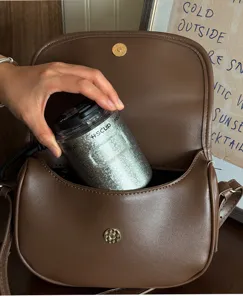 Close-up view of a portable stainless steel coffee cup placed inside a stylish brown leather bag.
