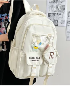 White Ita backpack detail showing clear window pocket, cute plush pendants and functional design.