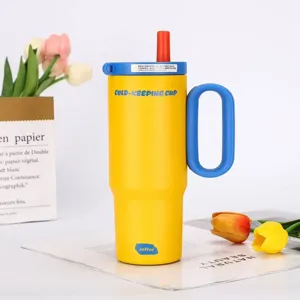 Detail view of yellow insulated tumbler with blue handle and straw, set in a clean floral scene.