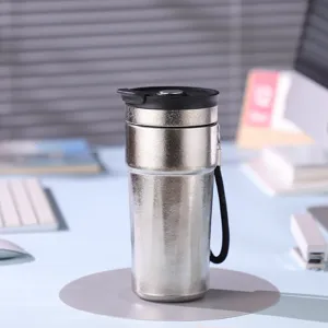 Gros plan détaillé du gobelet thermos en titane argenté avec couvercle noir sur le bureau de travail.
