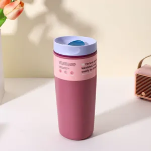 Close-up detail of a pink stainless steel insulated travel coffee mug with a purple lid on a clean table.