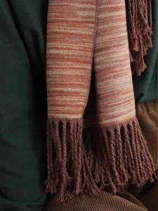 Detailaufnahme der weichen Stricktextur und der Fransen eines gestreiften Winterschals.