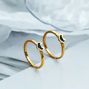 Zoom sur des bagues en acier titane doré avec motif ondulé et mini cadenas Ruyi noir.
