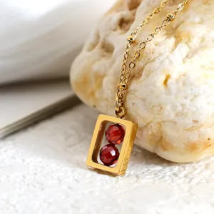 Detailopname van een geometrische gouden hanger met twee rode zirkoonkralen aan een ketting