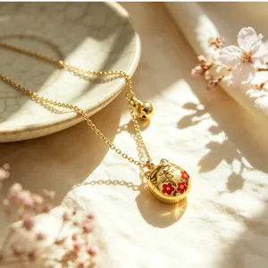 Primo piano di una collana con ciondolo a gatto della fortuna dorato e dettagli di fiori rossi