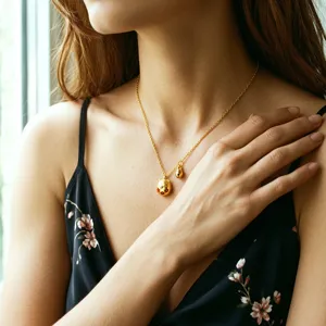 Dettaglio di una collana con ciondolo gatto portafortuna dorato e fiori rossi.