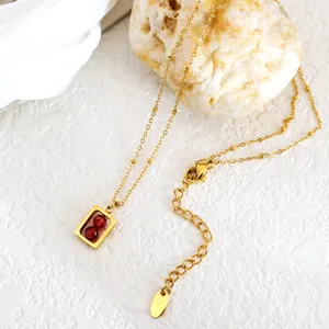 Detailweergave van een gouden titanium ketting met rechthoekige hanger en rode gezette stenen.