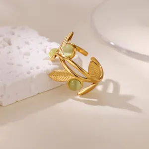 Close-up detail of gold leaf open ring with green zircon stones, elegant minimalist natural style.