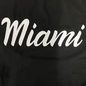 Detailansicht des schwarzen Badeanzugstoffs mit auffälligem weißen Miami-Städte-Schriftzug.