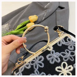 Close-up of vintage black floral clasp bag with golden ring handle and grey blazer background