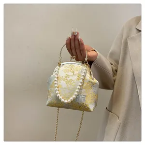 Close-up of vintage silk handbag with pearl handle and golden landscape pattern.