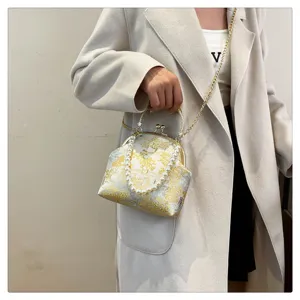 Close-up of elegant floral silk handbag with pearl handle and gold chain strap