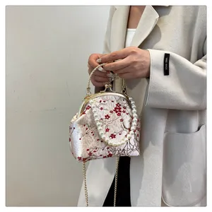 Macro view showing detailed red flower embroidery and elegant pearl handle on silk bag