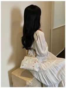 Dettaglio di una borsa a conchiglia ricamata con manici in bambù su una modella in bianco