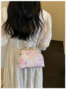 Vista dettagliata di una borsa a conchiglia ricamata in rosa con manico dorato su abito bianco