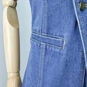 Denim vest pocket detail close-up showing fine yellow stitching and classic blue fabric texture.
