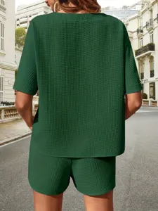 Detailed view of women's green textured short sleeve top and shorts set in outdoor street scene.