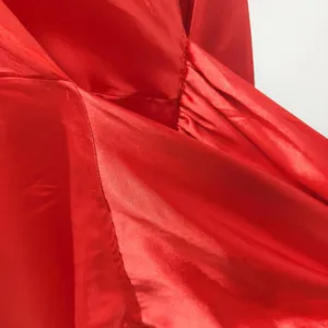 Close-up detail shot of red satin fabric, showing fine stitching and smooth texture.