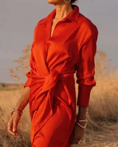 Close-up detail of the vibrant orange satin long-sleeve lapel jumpsuit in outdoor sunlight.