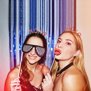 Two women wearing red crystal XOXO headbands at a festive party with photo props