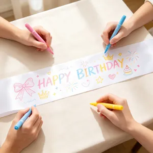 Des mains colorient une écharpe d'anniversaire en satin blanc DIY avec des feutres