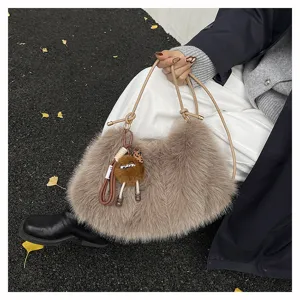 Model hält eine weiche graue Kunstfelltasche mit süßem Plüschanhänger im Freien