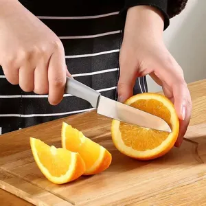 Détail de couteau à fruit en acier inoxydable avec poignée grise ergonomique coupant des oranges.