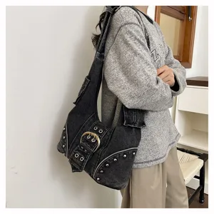 Detail view of a vintage distressed black denim underarm bag with punk rivets and large buckle