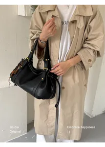 Dettaglio di borsa a secchiello in pelle nera vintage indossata con un trench beige