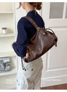 Vista lifestyle di borsa a spalla in pelle morbida marrone con coulisse indossata da modella