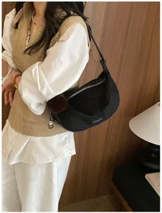 Elegante schwarze Hobo-Tasche in Halbmondform mit Bommel an der Schulter des Models