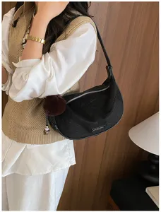 Schwarze Hobo-Tasche mit Pelz-Bommel-Anhänger an der Schulter des Models