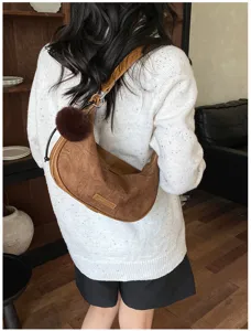 Detailansicht einer braunen Retro-Hobo-Tasche in Knödelform mit Fellanhänger auf weißem Pullover.