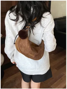 Rückansicht eines Modells mit einer braunen Wildleder-Halbmondtasche und Bommel-Anhänger