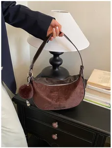 Elegante braune Vintage-Wildleder-Schultertasche mit Bommel auf einem Retro-Nachttisch