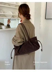 Λεπτομέρεια καφέ σουέτ τσάντας με κορδόνι, φορεμένη από μοντέλο σε εσωτερικό χώρο σπιτιού