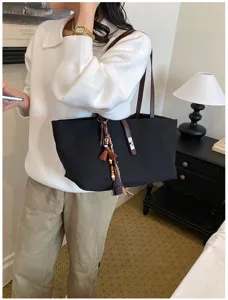 Bolso tote de lona negra con correas de cuero marrón y dijes decorativos de borlas