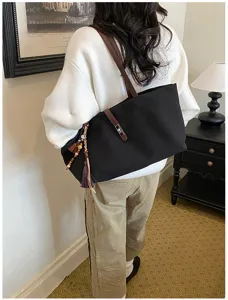Bolso tote grande de lona negra con correas de cuero y detalle de borla en una modelo