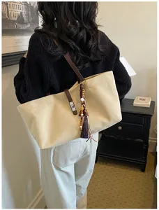 Vista detallada de un bolso tote de lona beige con correa de cuero y borla decorativa