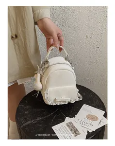 Elegante mini mochila blanca con ribete de encaje y lazo decorativo, sostenida por la mano