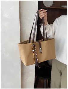 Vista detallada del bolso tote de lona con correas de cuero y borlas decorativas.