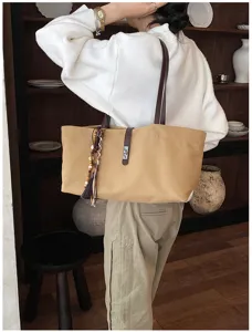 Vista trasera de un bolso tote de lona caqui con correas de cuero y una borla