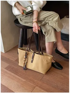 Detalle de un bolso tote grande de lona con asas de cuero y un elegante adorno de borla.