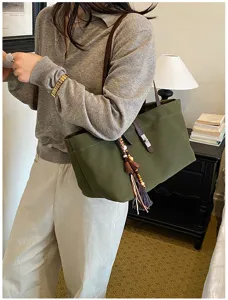 Detalle de bolso tote de lona verde oscuro con correa de cuero y flecos decorativos