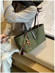 Primer plano de un bolso tote de lona verde con correas de cuero y borlas modernas.