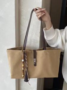 Bolso tote grande de lona con correas de cuero y adornos de borlas decorativas.
