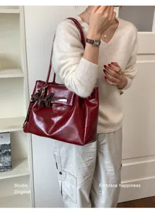 Modische rote Vintage-Einkaufstasche aus glänzendem Leder mit Schmetterlingsanhänger am Modell.