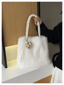 Nahaufnahme einer weichen weißen Plüschtasche mit geflochtenen Henkeln und einem Bärenanhänger.
