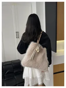 Modell trägt eine flauschige beige Schultertasche aus Kunstpelz mit geflochtenem Riemen