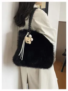 Nahaufnahme einer stylischen schwarzen Kunstfelltasche mit Flechtgriff und süßem Anhänger.